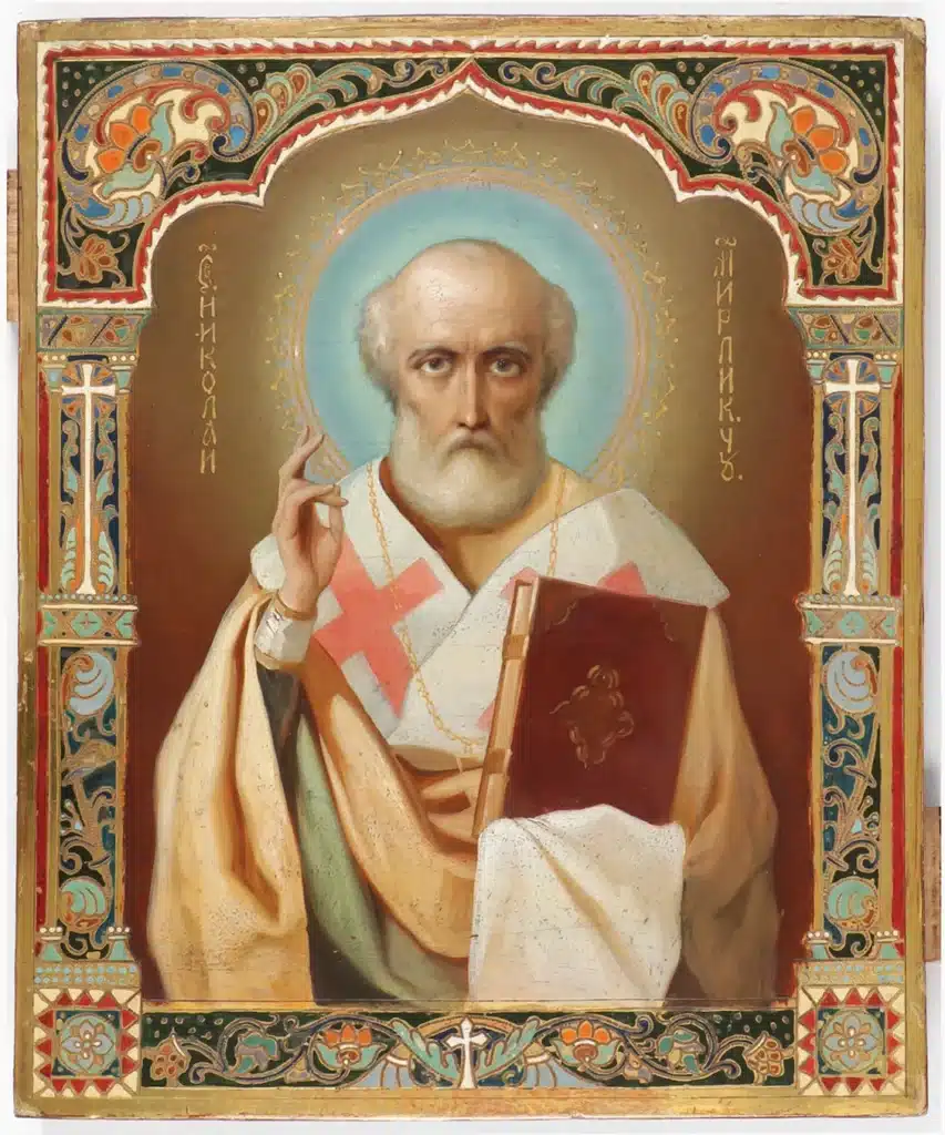 A traditional Orthodox icon of Saint Nicholas, depicted with a white beard, holding a Gospel book and making a blessing gesture, surrounded by a golden halo and ornate floral border.